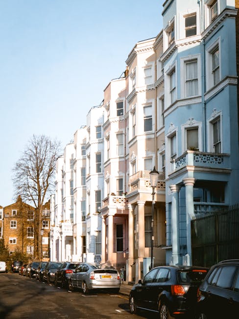 A row of multi-storey terraced houses with Victorian architectural features, painted in pastel shades including pink, blue, white, and cream, with decorative window trims and balconies. The buildings 
